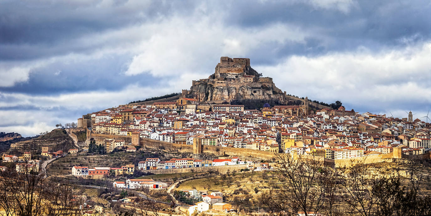 En el extremo norte de la Comunidad Valenciana, en la provincia de Castellón y a unos sesenta kilómetros de la costa, se encuentra Morella. Sus murallas centenarias dibujan una imagen icónica en un lugar estratégico, coronadas por un castillo a más de mil metros de altura. Alberga dieciséis torres, seis portales y cerca de dos kilómetros de paredes altas, todo ello declarado conjunto histórico-artístico y Patrimonio por la Unesco.