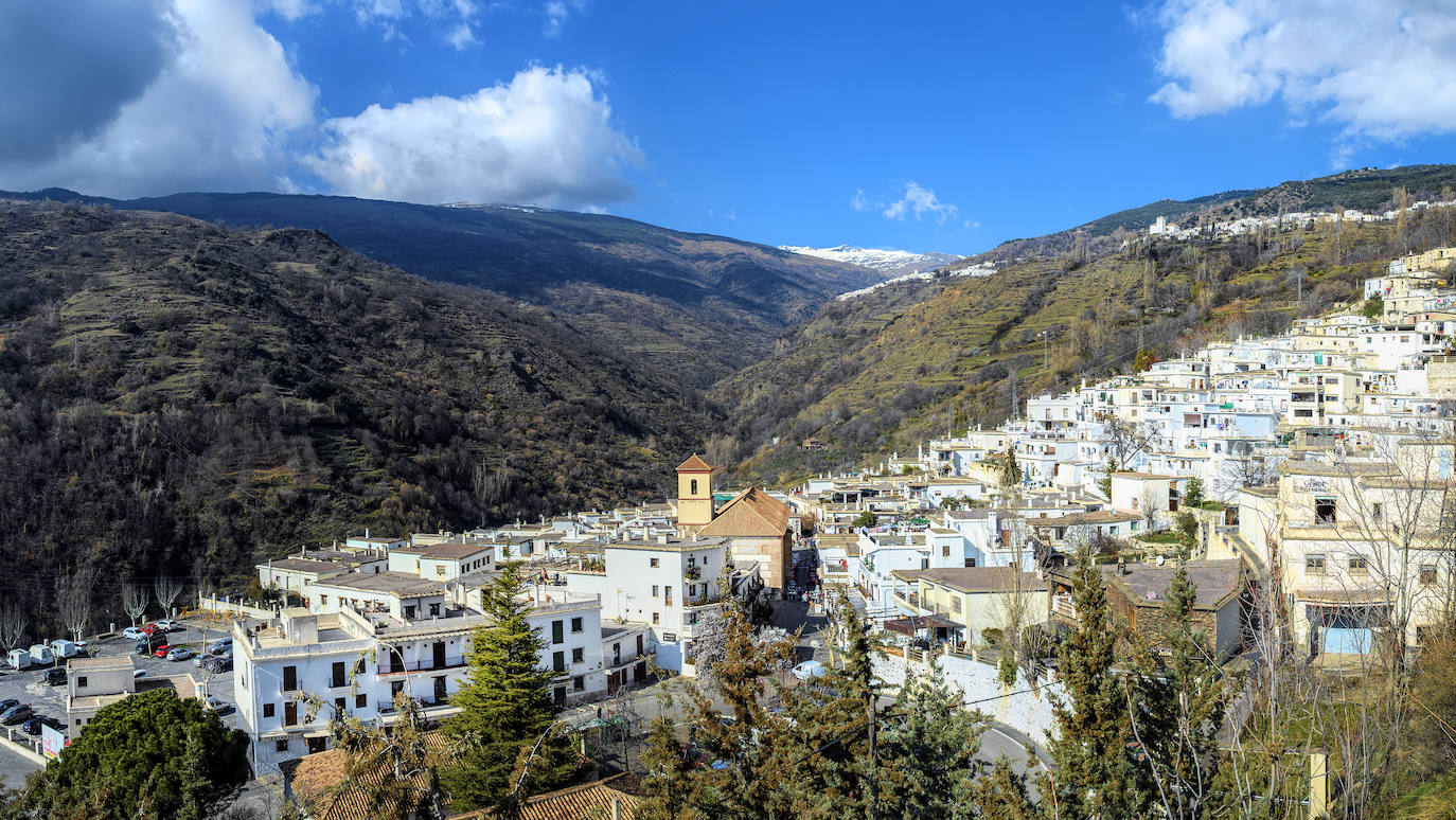 Pampaneira, Granada.  En las Alpujarras, una visita ineludible es el Valle del Poqueira, un paisaje encantador dibujado sobre el río que lleva el mismo nombre. En la ladera de una montaña se ubican tres pueblos preciosos. Pampaneira está catalogado como conjunto histórico-artístico, ha recibido numerosos galardones por su buen estado de conservación y varias guías lo incluyen sistemáticamente entre los sitios más bonitos de España. Destacan sus tinaos, casas blancas que tienen como particularidad el que tienen vigas al descubierto, al modo de los cobertizos, para unir los dos lados de la calle.