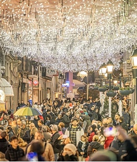 Imagem Secundária 2: Moradores celebram o Natal em evento vespertino (acima); o trem histórico da Vogue (canto inferior esquerdo); e uma das ruas do centro da cidade com guarda-chuvas e luzes de Natal (canto inferior direito)