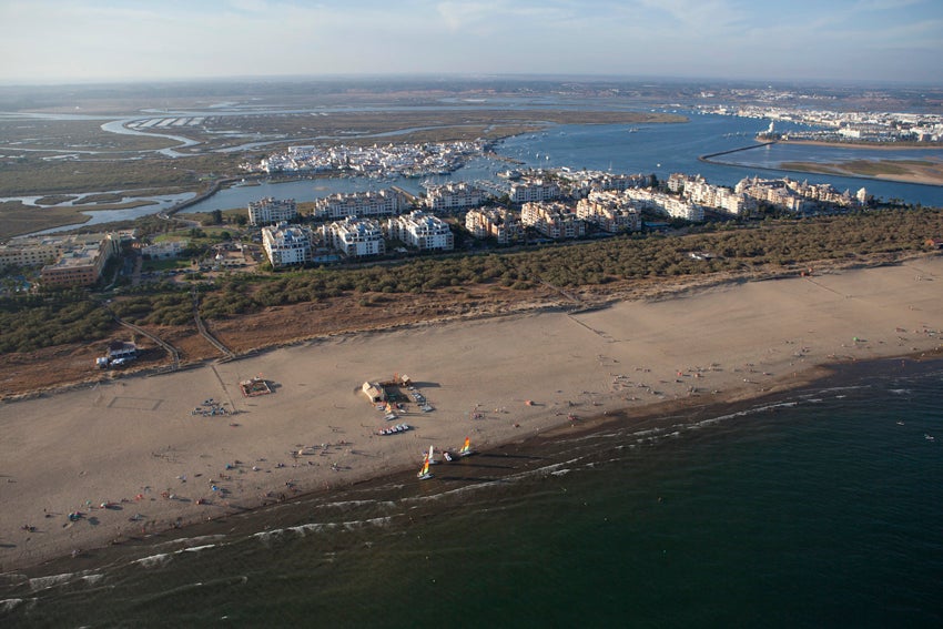 Vista aérea de la Playa de Punta del Moral, con su paseo marítimo tras las dunas y la vegetación