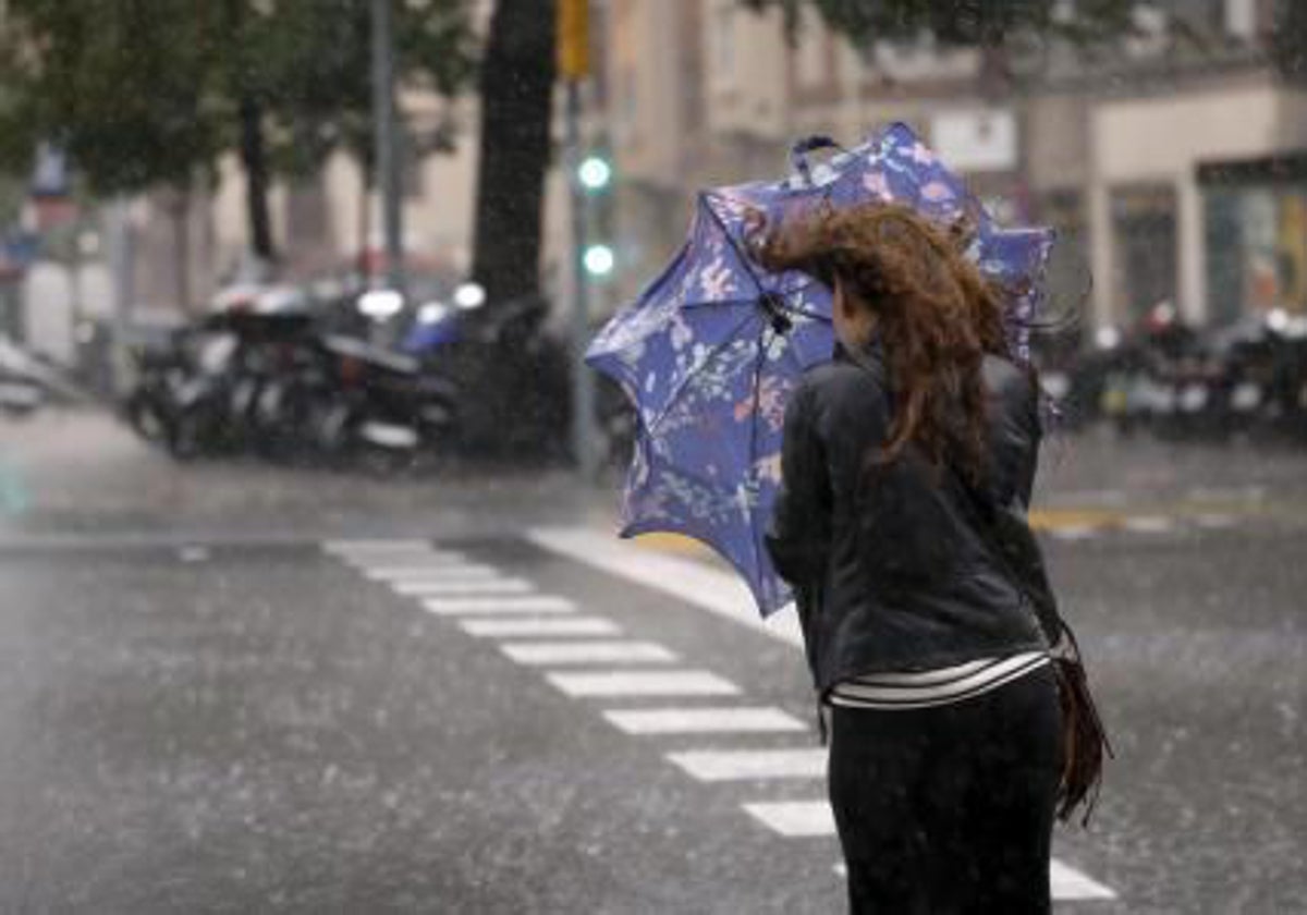 Una mujer bajo la lluvia con el paraguas roto por el viento