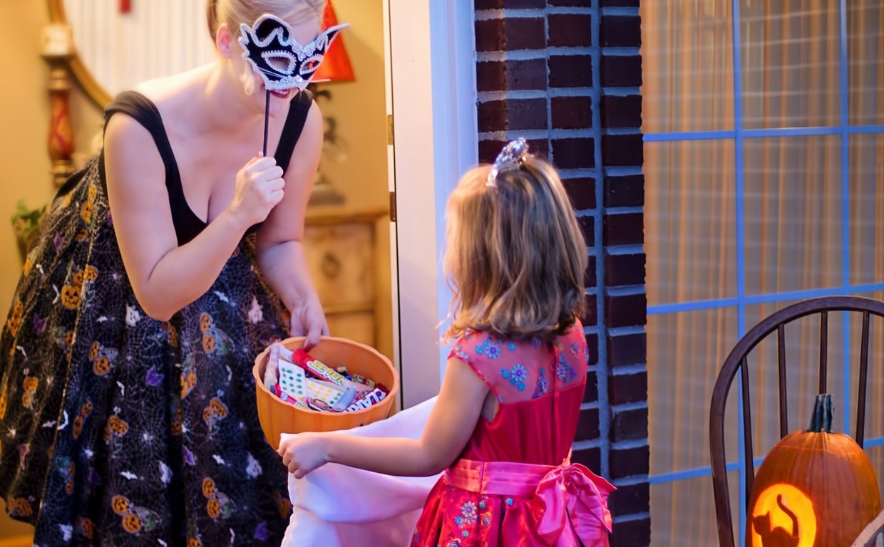 Niña pidiendo truco o trato en una casa por Halloween