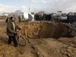 Un hombre pasea con su bicicleta junto con un túnel recién destruido, en la zona fronteriza entre la Franja de Gaza y Egipto. / Ap