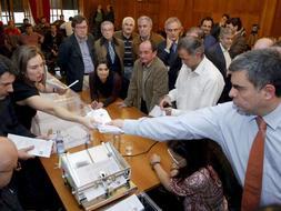 El presidente de la Junta Electoral Provincial de Orense, Fernando Alañón (d), entrega un montón de votos a la secretaria de la junta para pasarlos por la máquina contadora, durante el escrutinio de los votos procedentes de la emigración. /Efe