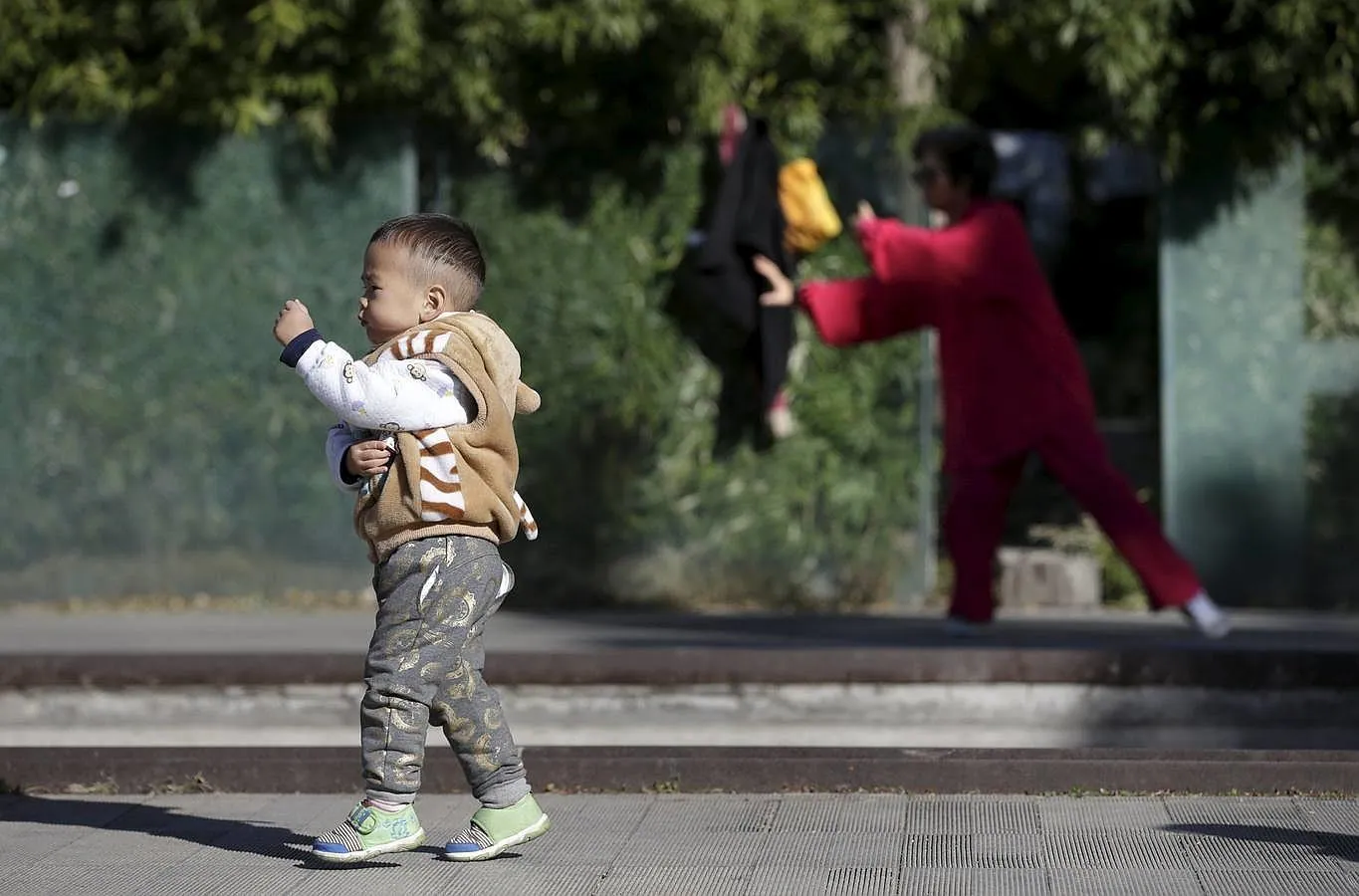 Un niño juega mientras una mujer practica Taiji, una disciplina de las artes marciales, en una zona residencial de Beijing 
