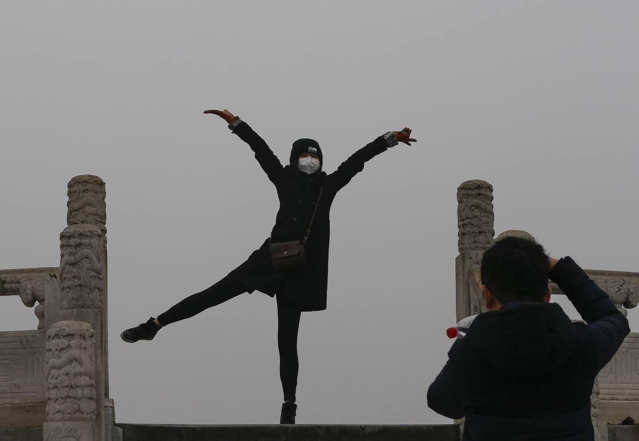 Una mujer posa para una foto mientras usa una mascarilla para protegerse contra la contaminación ambiental durante una visita al Templo del Cielo de Pekín (China)