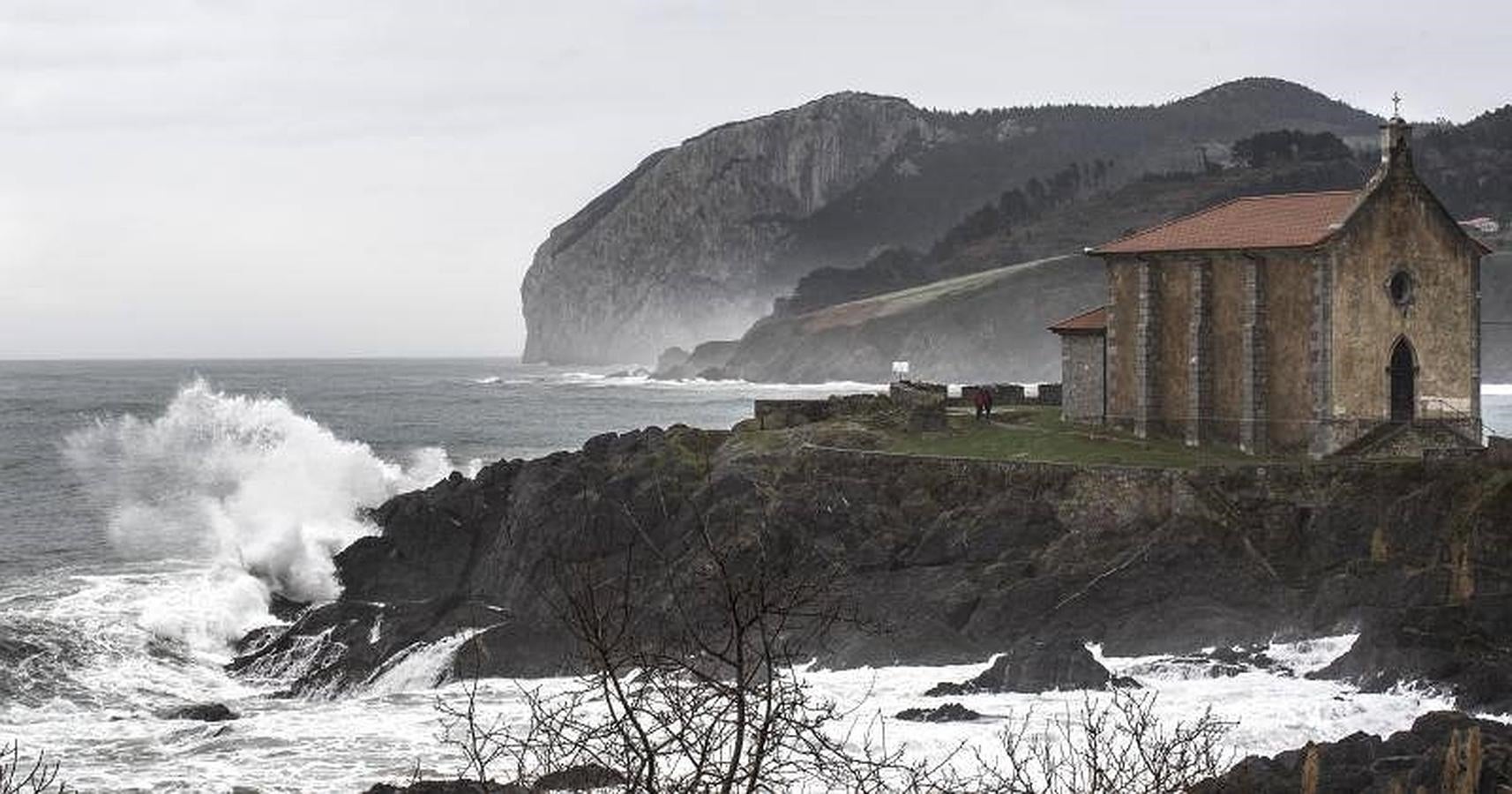 Una pareja pasea junto a la ermita de Santa Catalina en Mundaka (Vizcaya) en la mañana de hoy, durante la cual el Gobierno Vasco ha rebajado el nivel de alerta por oleaje tras la pleamar. 