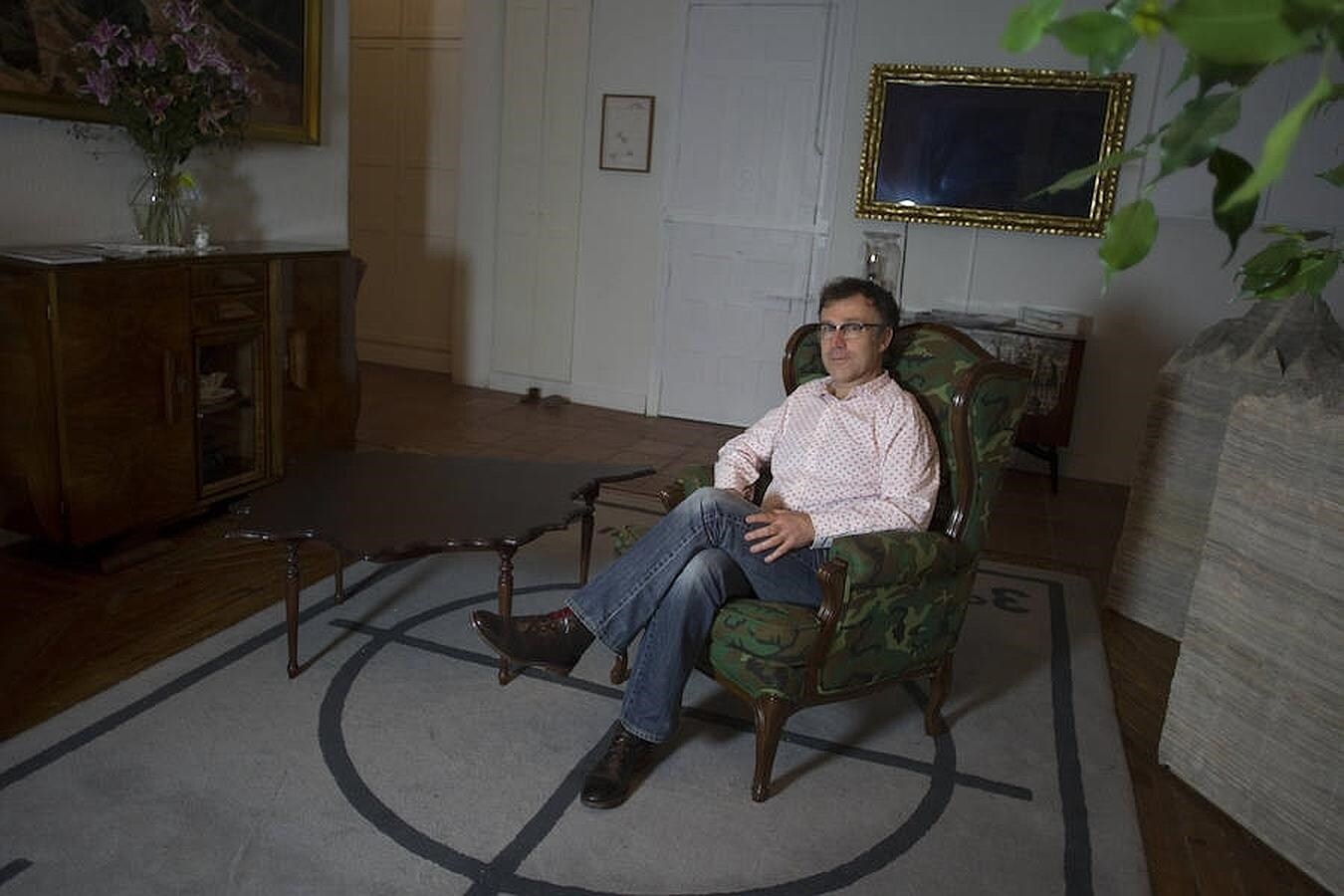 El artista descansa en su sofá de camuflaje, junto a una de sus mesas con la silueta de la Península Ibérica y una de sus alfombras