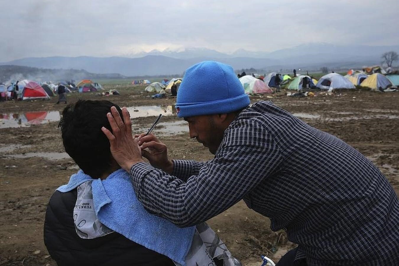 Un refugiado afeita a otro en el campamento de Idomeni, (Grecia, frontera con Macedonia)