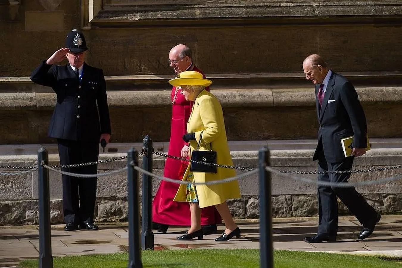 La Reina recibe el saludo de un policía mientras es acompañada en los alrededores de la capilla por el obispo David Conner.. 