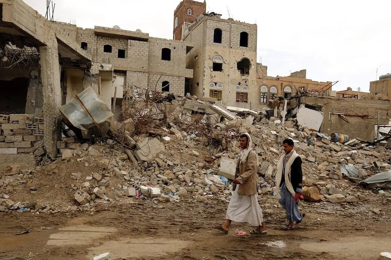 Dos hombres pasan por delante de las ruinas de un edificio destruido por un bombardeo de la coalición árabe liderada por Arabia Saudí en Saná, Yemen