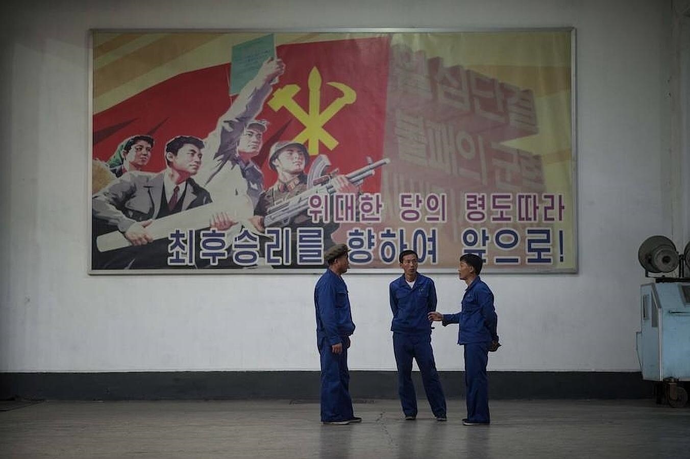 Trabajadores de una fábrica de Pyongyang visitada por medios extranjeros, delante de propaganda del régimen de Kim Jong-un