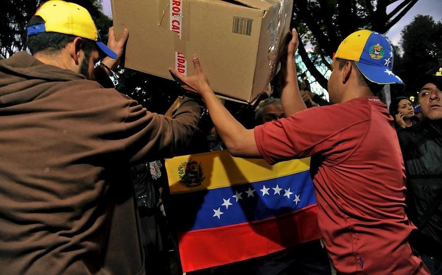 Dos hombres organizan la recogida de productos que serán destinados a la población venezolana que viven en peores condiciones. Debajo la bandera de Venezuela. 
