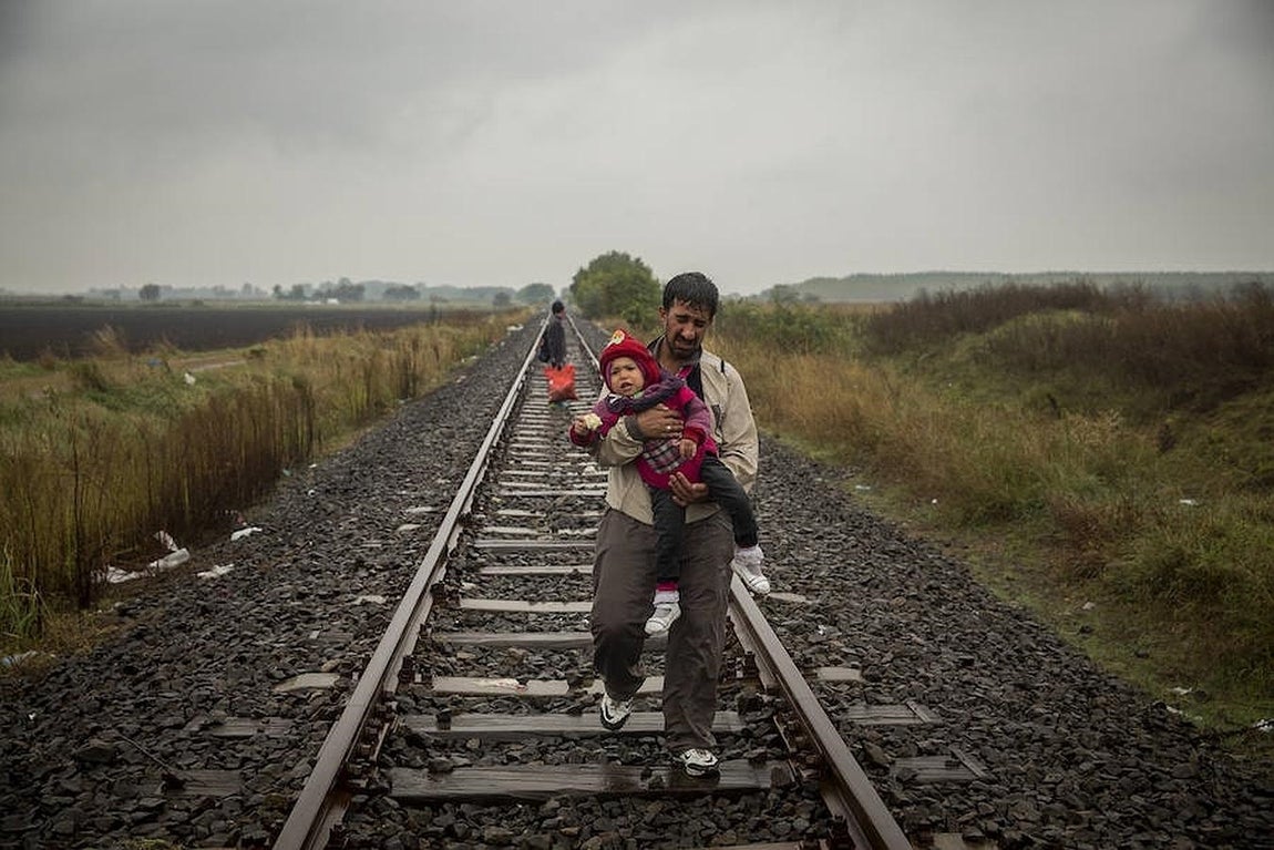 Un padre camina por las vías del tren con su hijo en brazos después de cruzar la frontera entre Serbia y Hungría.. 