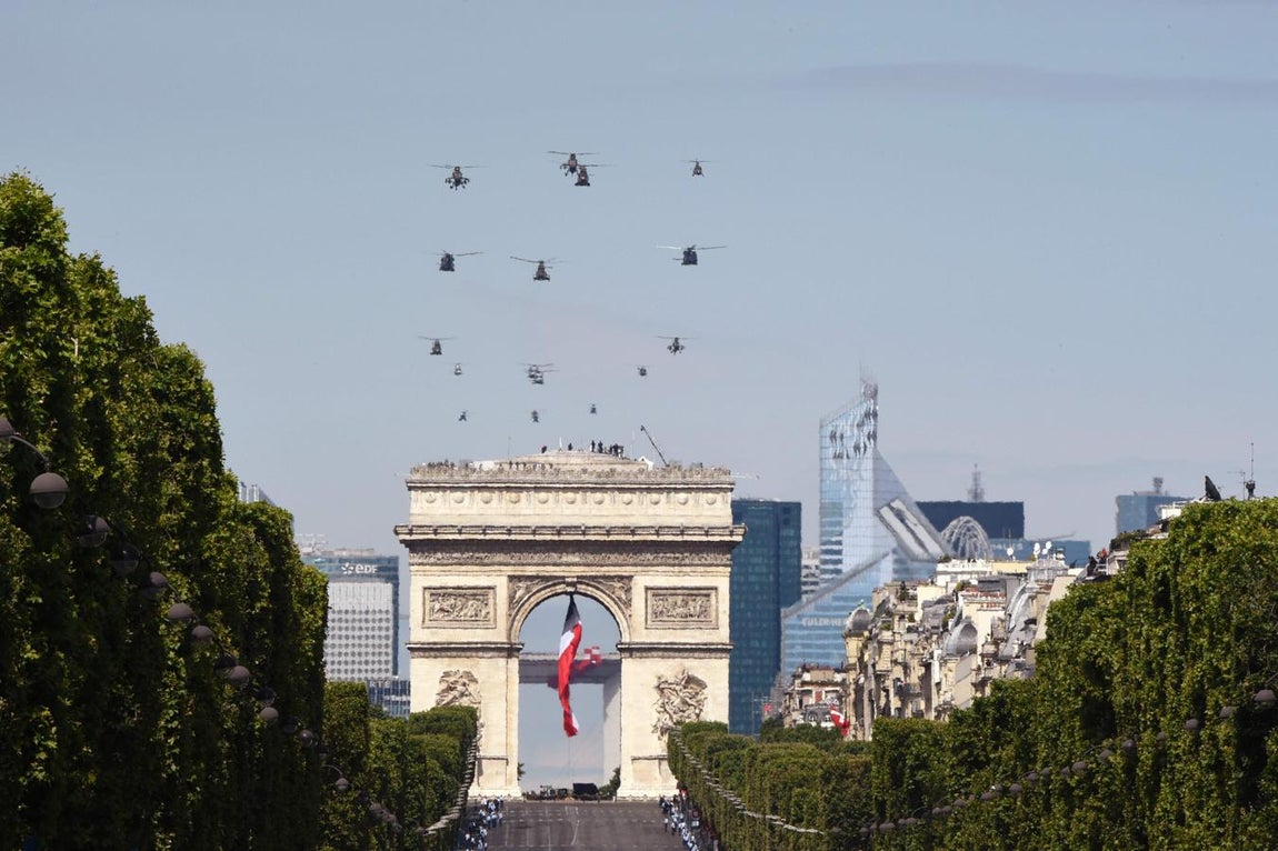 Sobre el Arco del Triunfo de París, adornado con una bandera de Francia, sobrevuelan varios helicópteros antes de que empiece el desfile militar con motivo del Día de la Bastilla. 