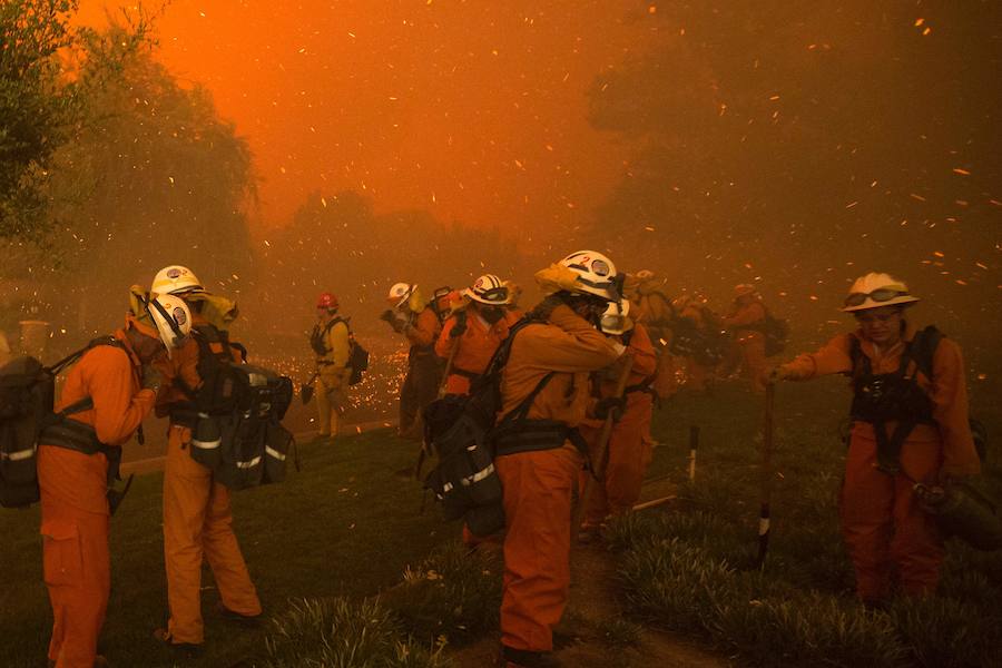 Un equipo de bmberos se protegen de las brasas y el humo a la vez que las llamas se acercan a las viviendas en Santa Clarita. 