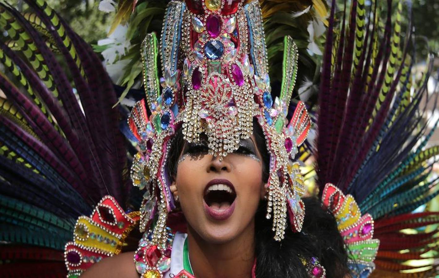 Una mujer luce una gran corona multicolor rodeada de plumas. 