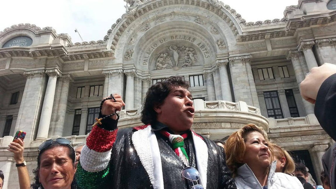 Un hombre vestido al estilo del fallecido cantautor mexicano Juan Gabriel canta junto a cientos de personas que lloran y entonan sus canciones a las afueras de Palacio de Bellas Artes, en Ciudad de México. 