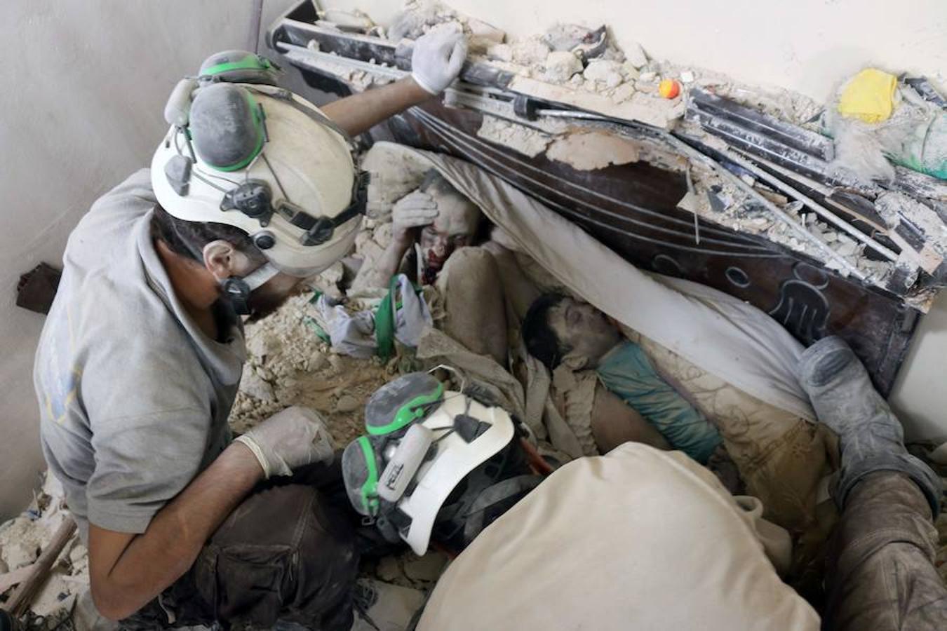 Voluntarios de protección civil de Siria, conocidos como los Cascos Blancos, recuperan cuerpos de entre los escombros de un edificio tras un ataque aéreo 
