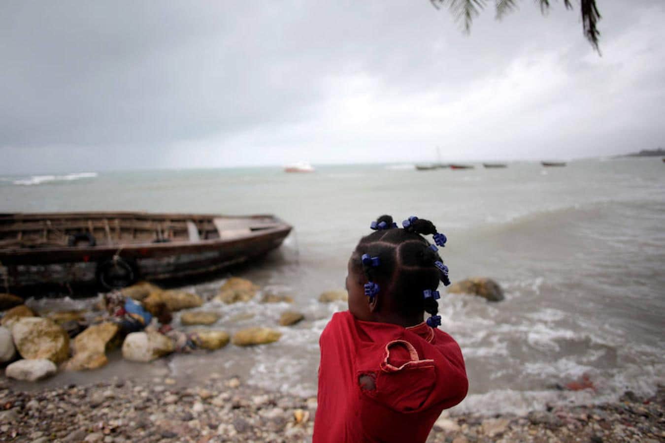 Una niña mira un barco en la playa mientra que el huracán se aproxima