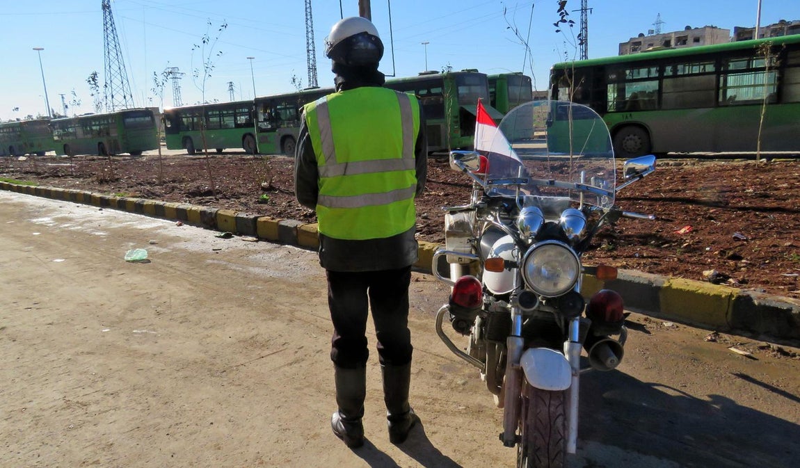 Un policía fiel a Al Assad espera junto a los autobuses preparados para trasladar a los rebeldes sirios y sus familias fuera de Alepo. 