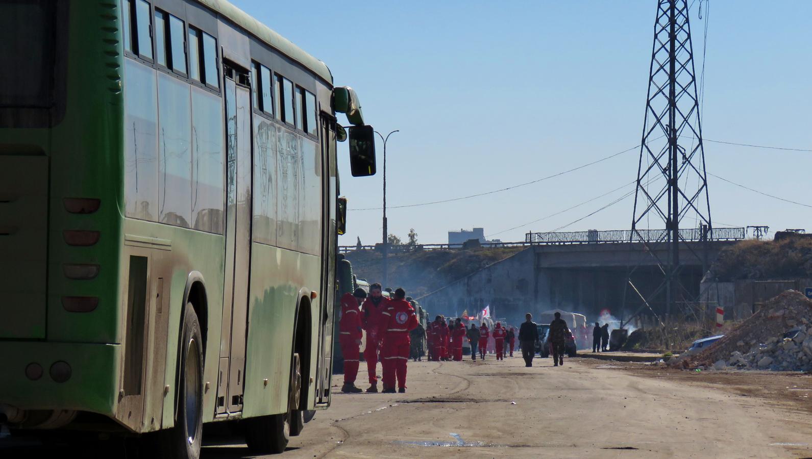 Un grupo de miembros de la Media Luna Roja espera junto a los autobuses preparados para evacuar de Alepo a los rebeldes sirios y sus familias. 