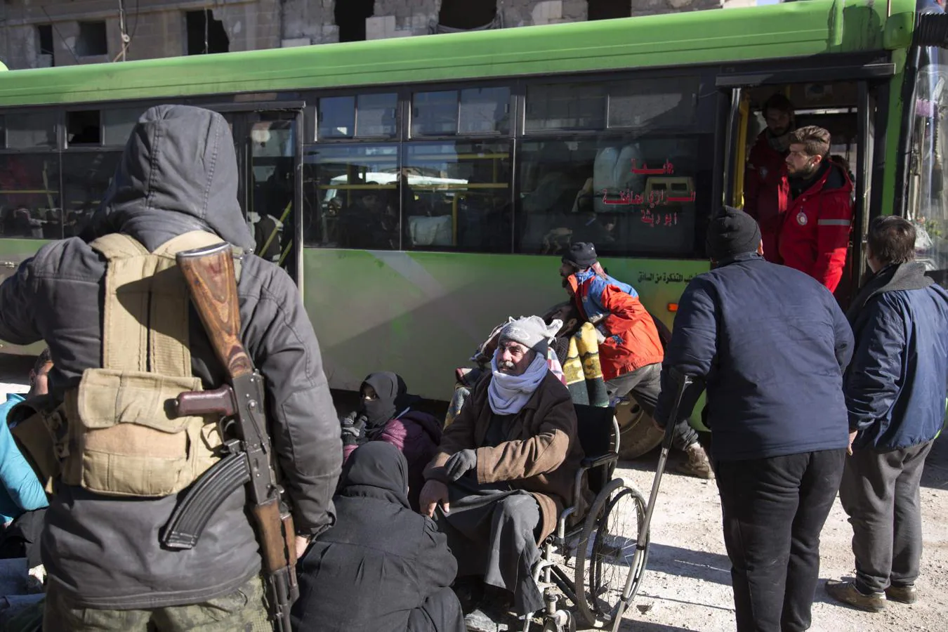 Un grupo de habitantes del este de Alepo junto a los autobuses preparados para la evacuación de los barrios del este de la ciudad siria. 