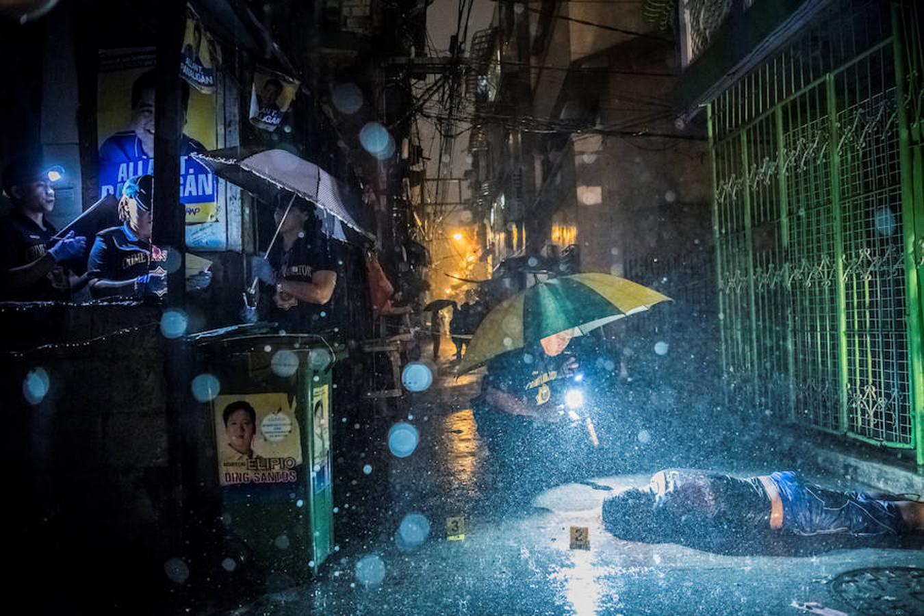 La Policía de Filipinas investiga un callejón de Manila en el que yace un cadáver bajo la intensa lluvia. 