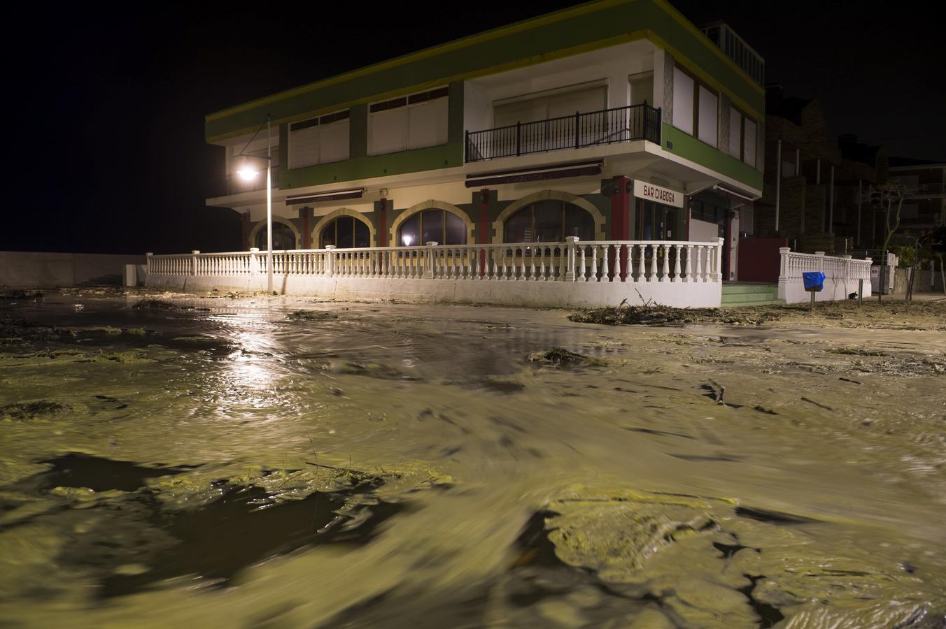 Una calle próxima a la playa de la Concha en Suances cubierta de espuma del mar y palos arrastrados por la marea. 