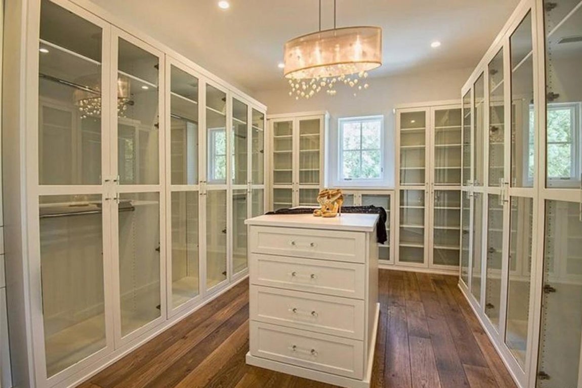 Vestidor con armarios de cristal e isla con cajones en el medio.