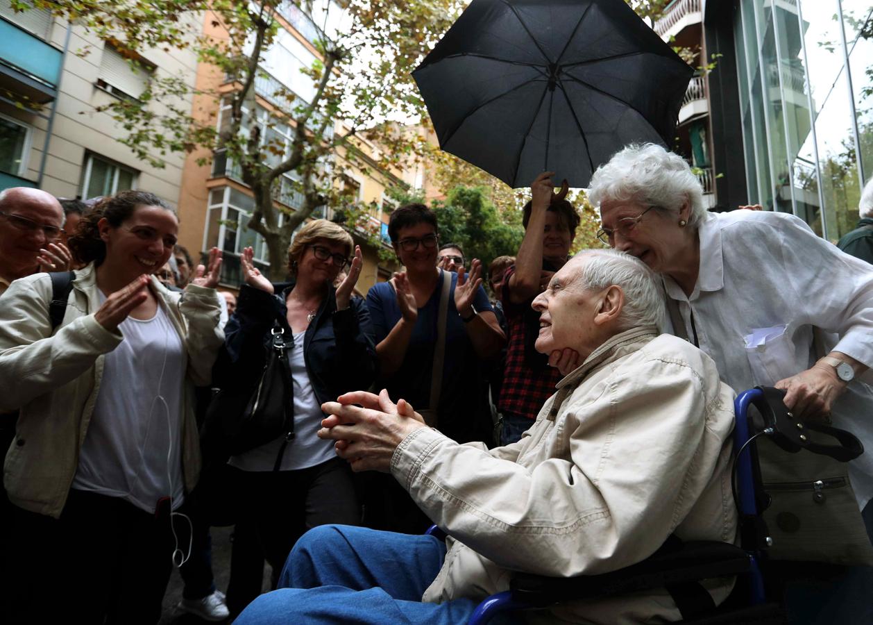 Un abuelo, en silla de ruedas, sale del un colegio aplaudido por decenas de personas. 