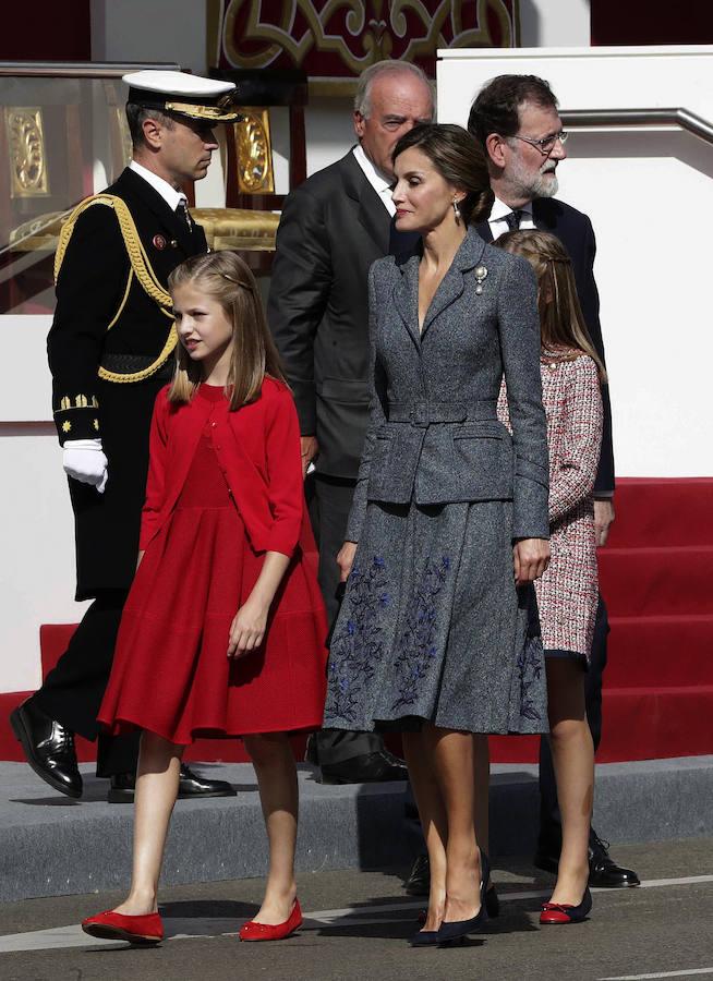 Este 12 de octubre, Doña Letizia ha vuelto a apostar por su diseñador fetiche, Felipe Varela. La Reina ha optado este año por un traje de chaqueta gris azulado con un bordado en la falda y un broche con perla en la solapa, además del cabello recogido. 