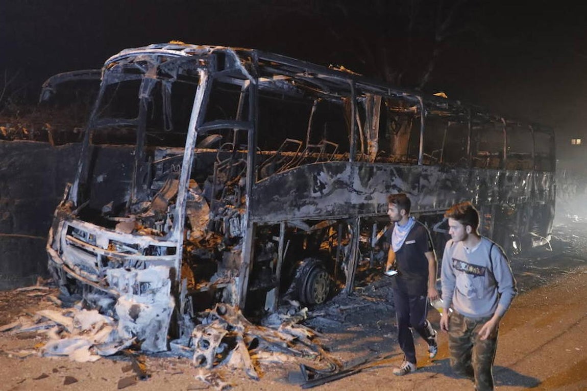 Dos jóvenes caminan junto a un autobús calcinado hoy en Chandebrito, Galicia (España). 