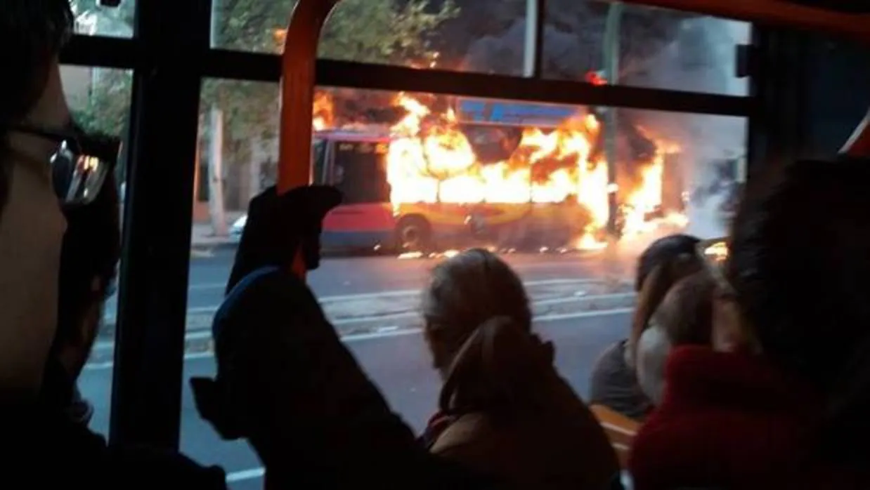 Pasajeros de un autobús de Tussam observan como se incendia otro vehículo de la empresa.