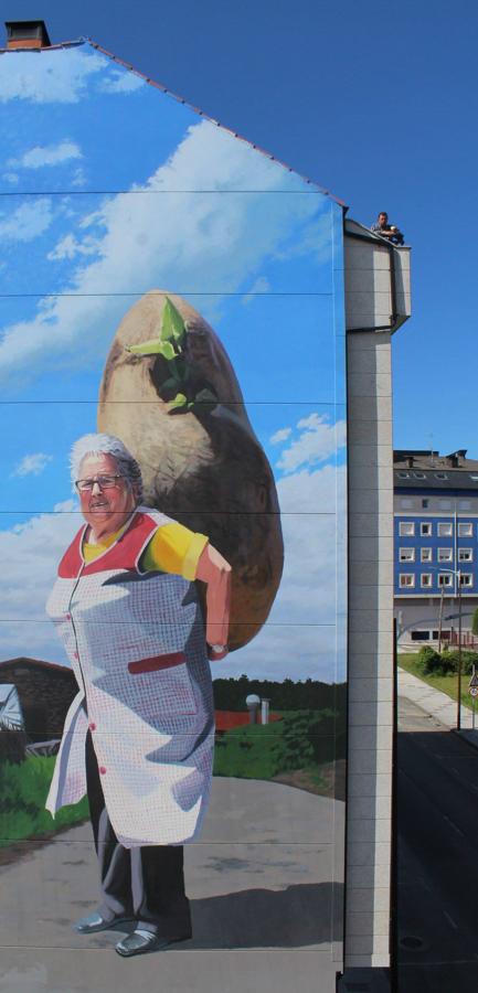 Las patatas-menhir de Carballo. «Carballo es tierra de patata, tanto que tiene una variedad autóctona, la Fina de Carballo. Desde que supe que iba a pintar en Carballo estuve buscando una señora de complexión fuerte. Quería cambiar el menhir de Obelix por una patata gigante.La modelo se llama Elisa, es la abuela de otro amigo. Fuimos un domingo hasta Arzúa a una comida familiar para sacar las fotos. Esa familia se dedicaba a la leche y todavía conservan las cuadras de la vacas. Me hablaron de las tasas de la leche, de la Unión Europea y de todos los requisitos que había que cumplir que hicieron que mucha gente que vivía del ordeño se quedase sin nada. Con Elisa me hubiese gustado hacer otra cosa, pero la fecha para el mural de Carballo se acercaba y necesitaba a mi 'Obelisa'.Tambien hablamos de la huerta, dijo: «En Galicia no crecían las cosas hasta que llegó el químico». ¿Qué será el químico?, pensé. Fue muy concreta al hablar de las diferentes mezclas de químicos (abonos) para los diferentes cultivos. De toda esa charla me quedé con la palabra Nitromón. El resultado es un juego entre Obelix y una mujer con Nitromón en el cuerpo que hace que sus patatas sean de tamaño de menhires«, explica el autor.