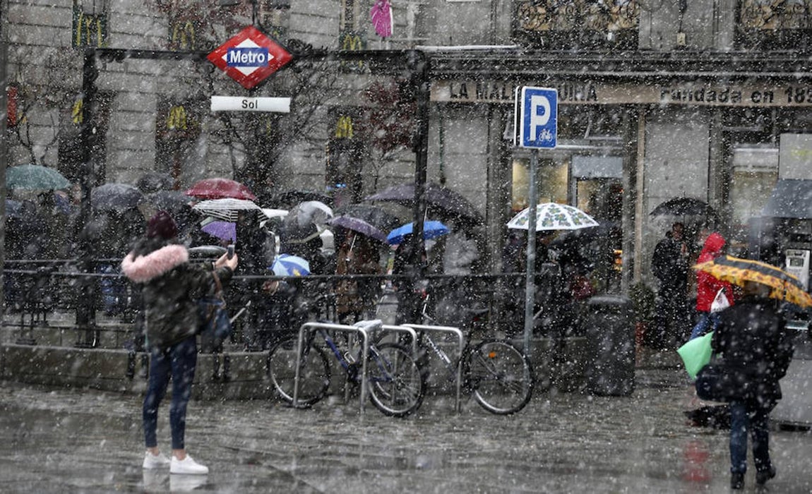 Los transeúntes caminan junto a la madrileña boca de metro de Sol y se cubren con paraguas para protegerse de la nevada.. 