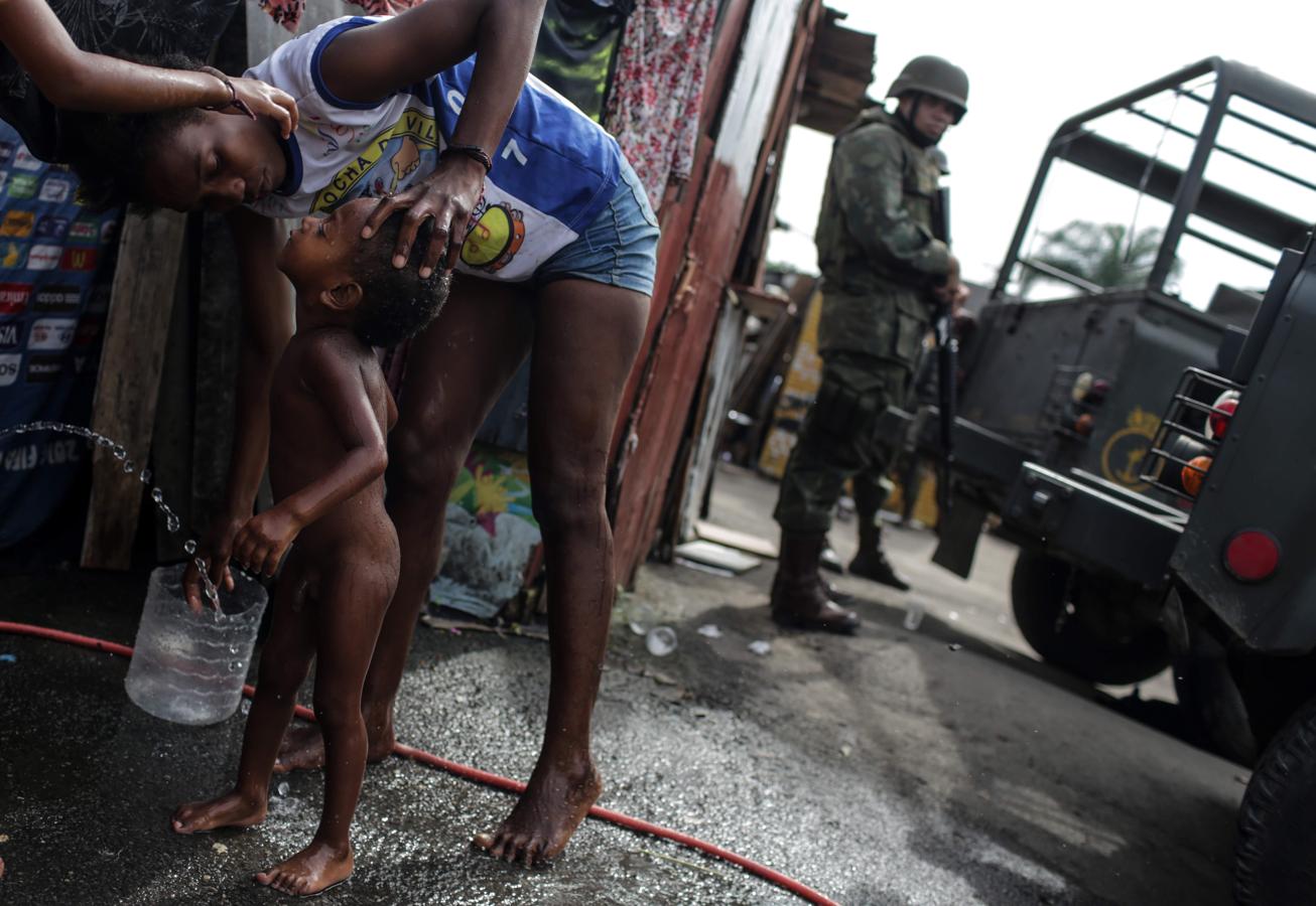 Una mujer baña a su niño ante la presencia de soldados del ejército brasileño. 