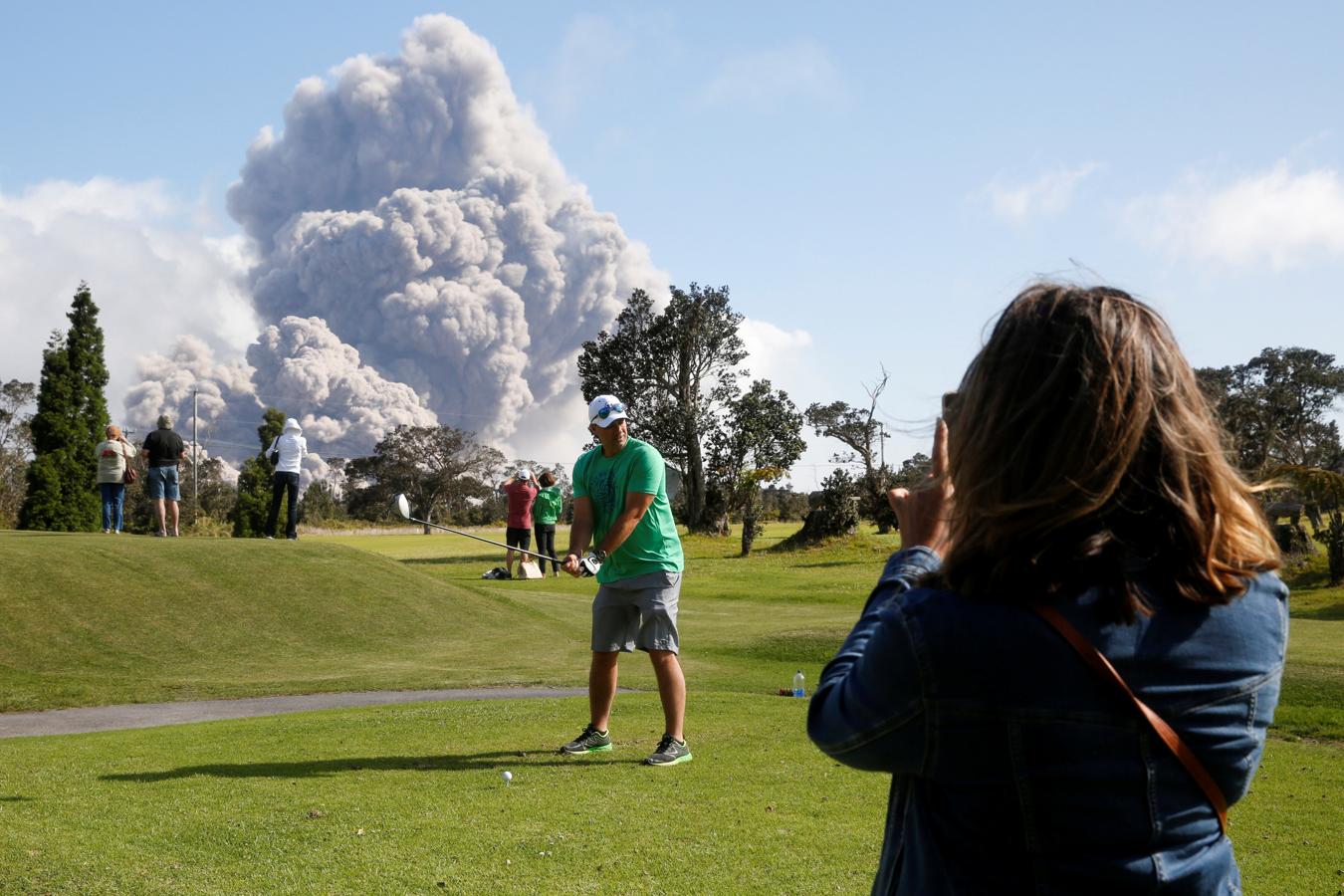 Un hombre juega al golf con la erupción de cenizas de fondo. 
