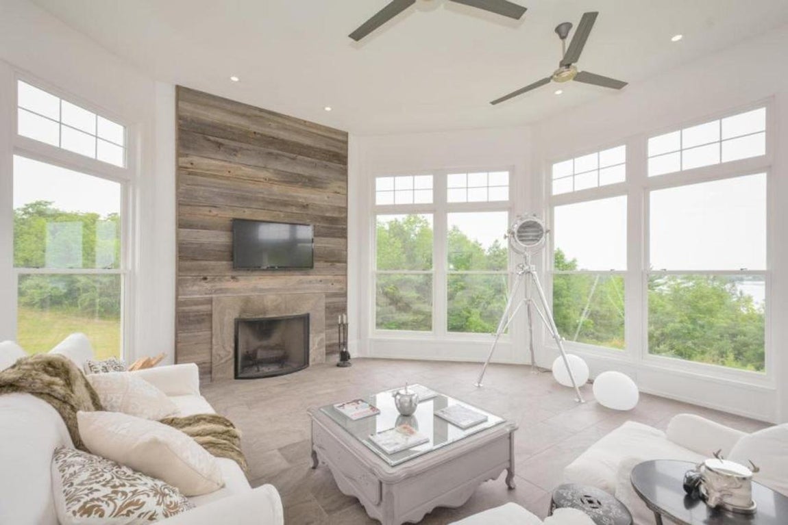 Sala de estar. La sala de estar es acristalada, muy luminosa y tiene suelos de madera. Su pared frontal está revestida en este material y tiene una gran chimenea