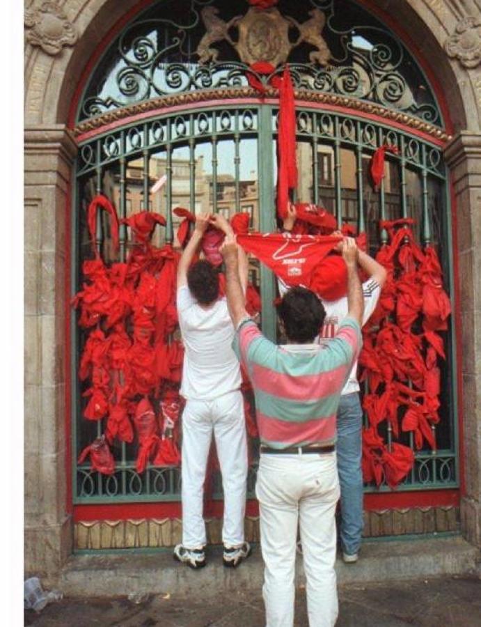 Varios pamploneses cuelgan su pañuelo rojo en la puerta del Ayuntamiento en San Fermín en señal de luto por Blanco. 