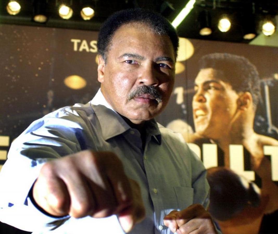 Muhammad Ali posando en cámara con una antigua fotografía suya de fondo. 