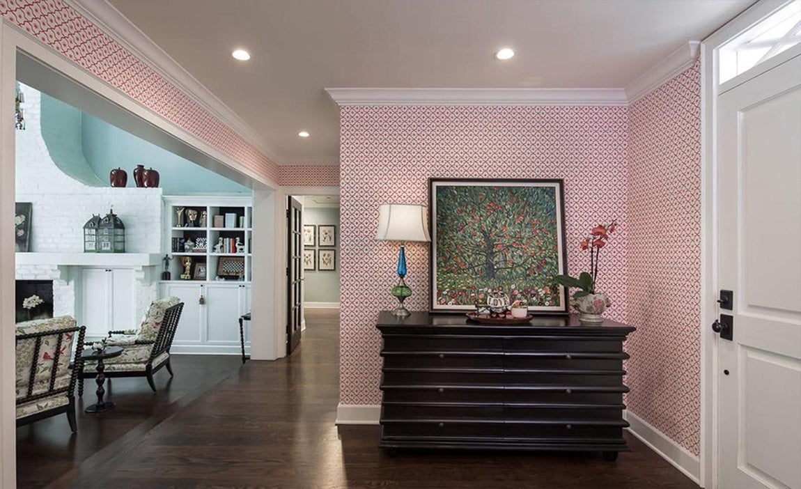 Recibidor. Según se abre la puerta principal lo que nos encontramos es con un vestíbulo pequeño pero suficiente, envuelto en papel geométrico rojo y blanco que da un toque de alegría al recibidor. Más adelante subiremos unos peldaños para adentrarnos en un salón y comedor donde se encuentra una chimenea asimétrica de ladrillos blancos flanqueada por vitrinas y armarios a medida.