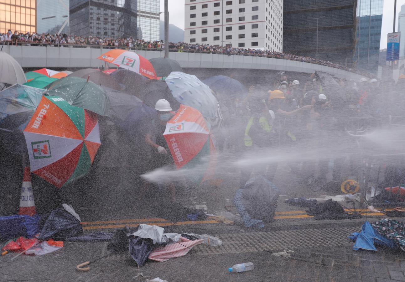 Varios manifestantes se protegen del lanzamiento de agua a presión por la Policía. Las autoridades han cargado contra los asistentes después de que estos aplazaran –y no retiraran, como pedían– el debate sobre la ley de extradición a Pekín.. 