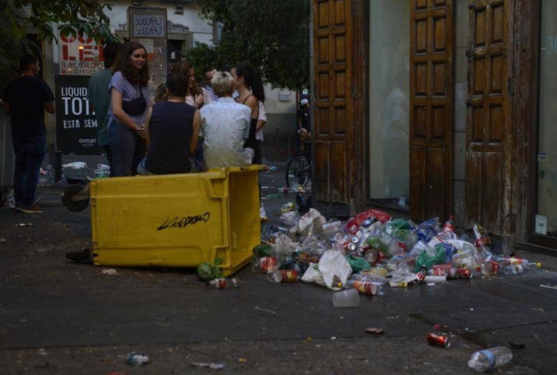 10. Jóvenes sentados esta madrugada, sobre un contenedor. En el suelo, la basura que contenía, esparcida por el suelo