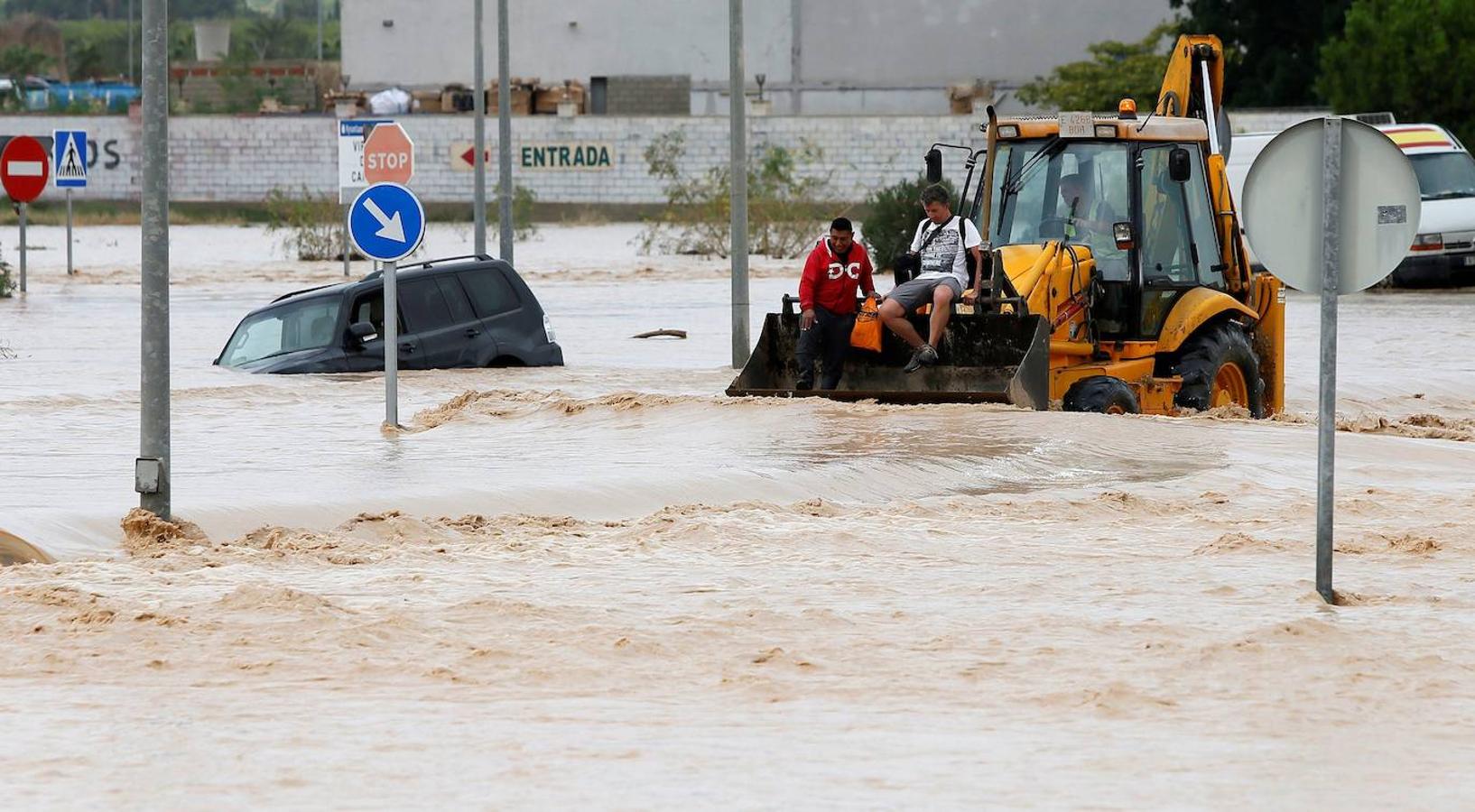 Dos ocupantes de un vehículo son rescatados con una pala mecánica, mientras la carretera permanece inundada por el efecto de las riadas, este viernes, en la ciudad alicantina de Orihuela, que se encuentra incomunicada, a causa del desbordamiento del río Segura. 