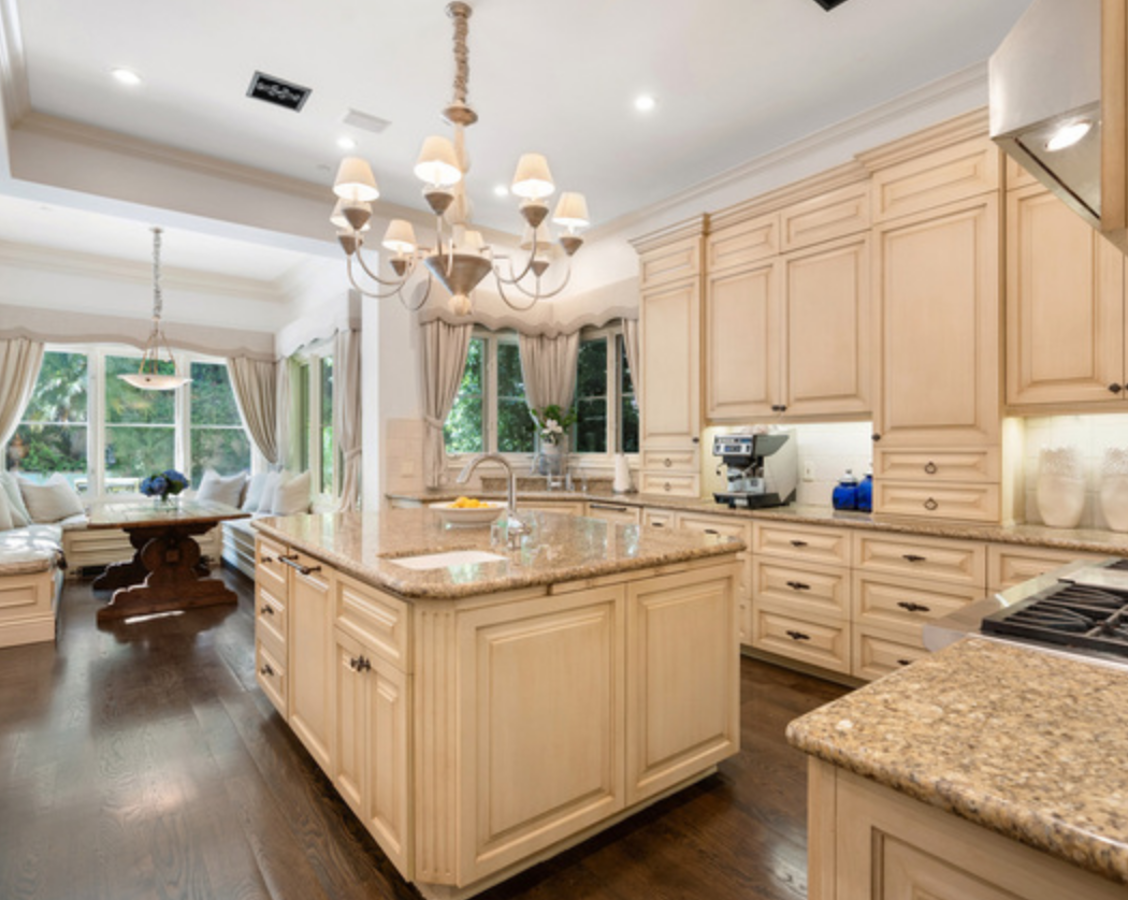 La mansión de Beverly Hills de Britney Spears. La cocina, muy amplia, cuenta con encimeras de granito y muebles de madera con numerosos espacios de almacenamiento. Destaca la isla central con fregadero y espacio para preparar la comida.