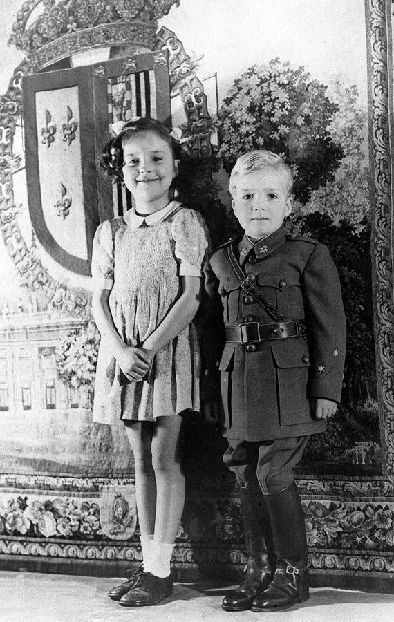 El Rey Juan Carlos de Borbón posa con el uniforme de capitán de caballería que le ha sido enviado de España, acompañado de su hermana, la Infanta Pilar, en 1942