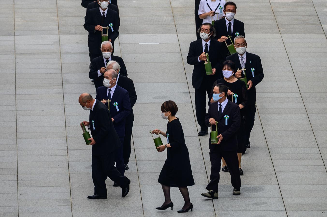 Un grupo de personas lleva pequeños jarrones con agua durante el acto en memoria de las víctimas de Hiroshima. 