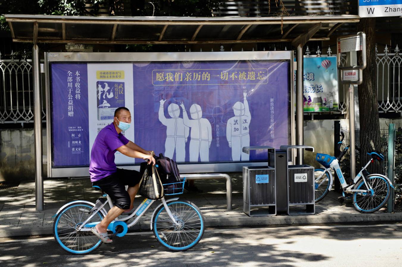 Un ciclista pasa ante una parada de autobús con un anuncio de un libro sobre la lucha contra la pandemia. 