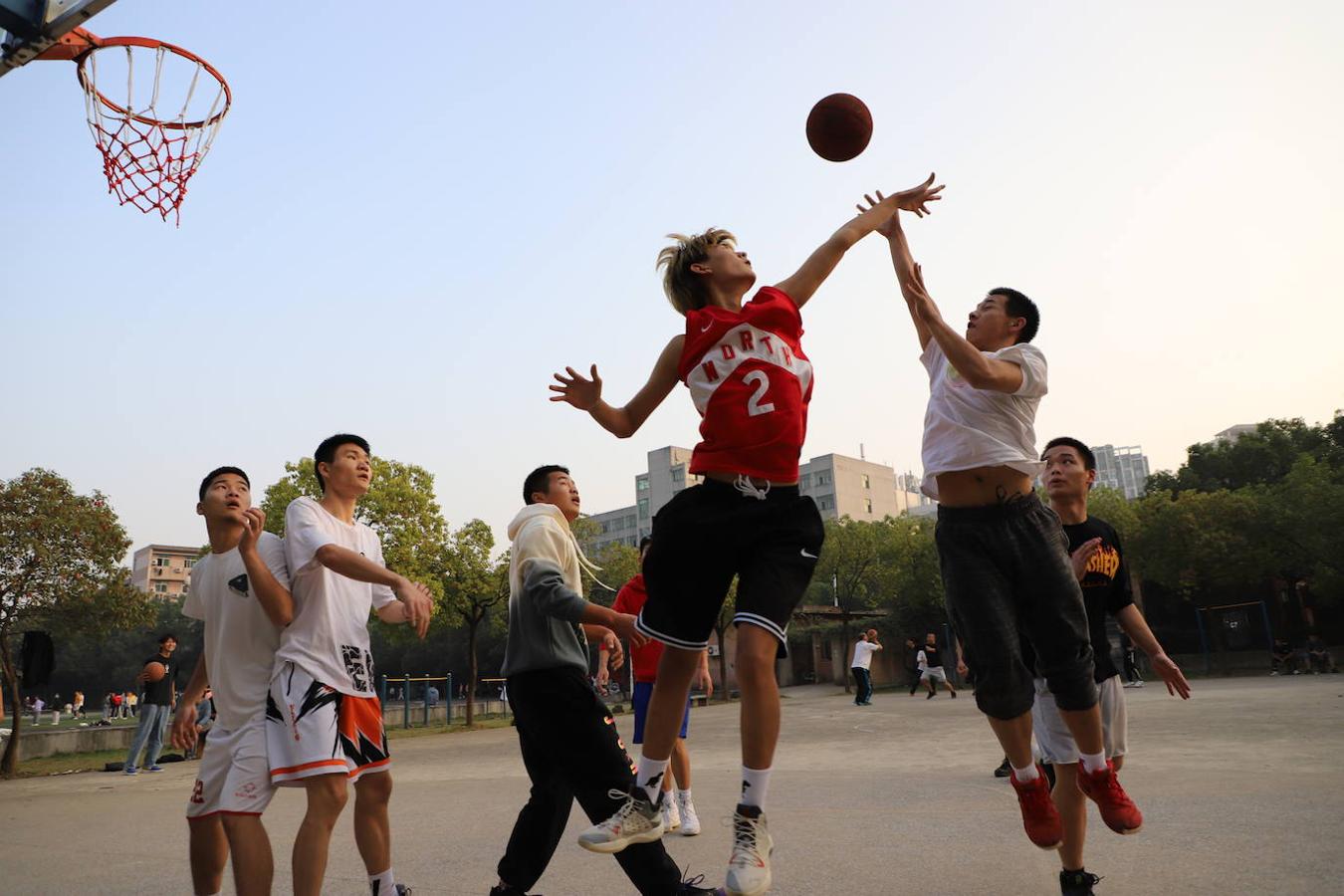 Sin mascarilla porque no se ha informado de casos de coronavirus desde antes del verano, un grupo de jóvenes juega al baloncesto en el campo de deportes de la Universidad Textil de Wuhan. 